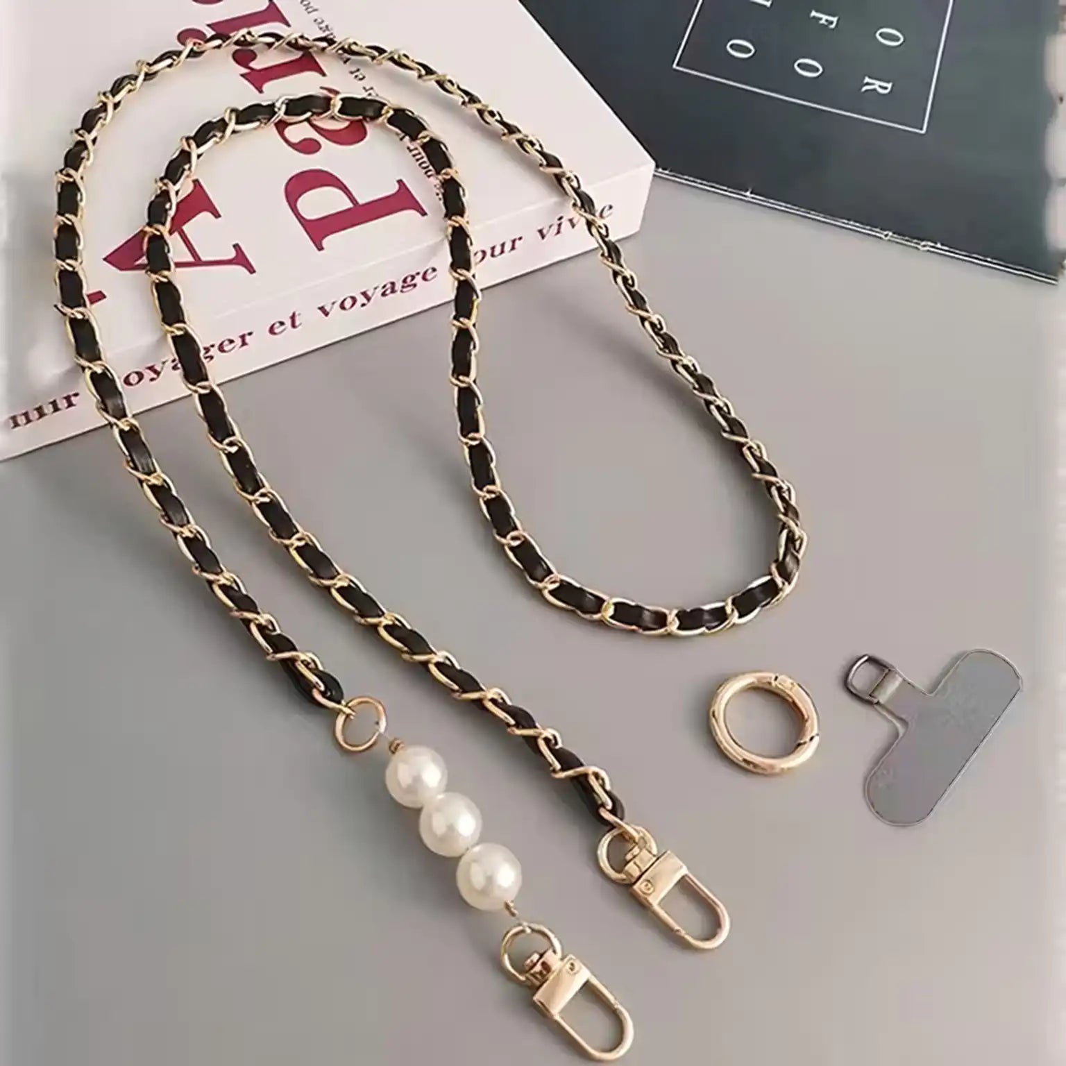 Gold and black chain strap with pearl accents on a gray surface