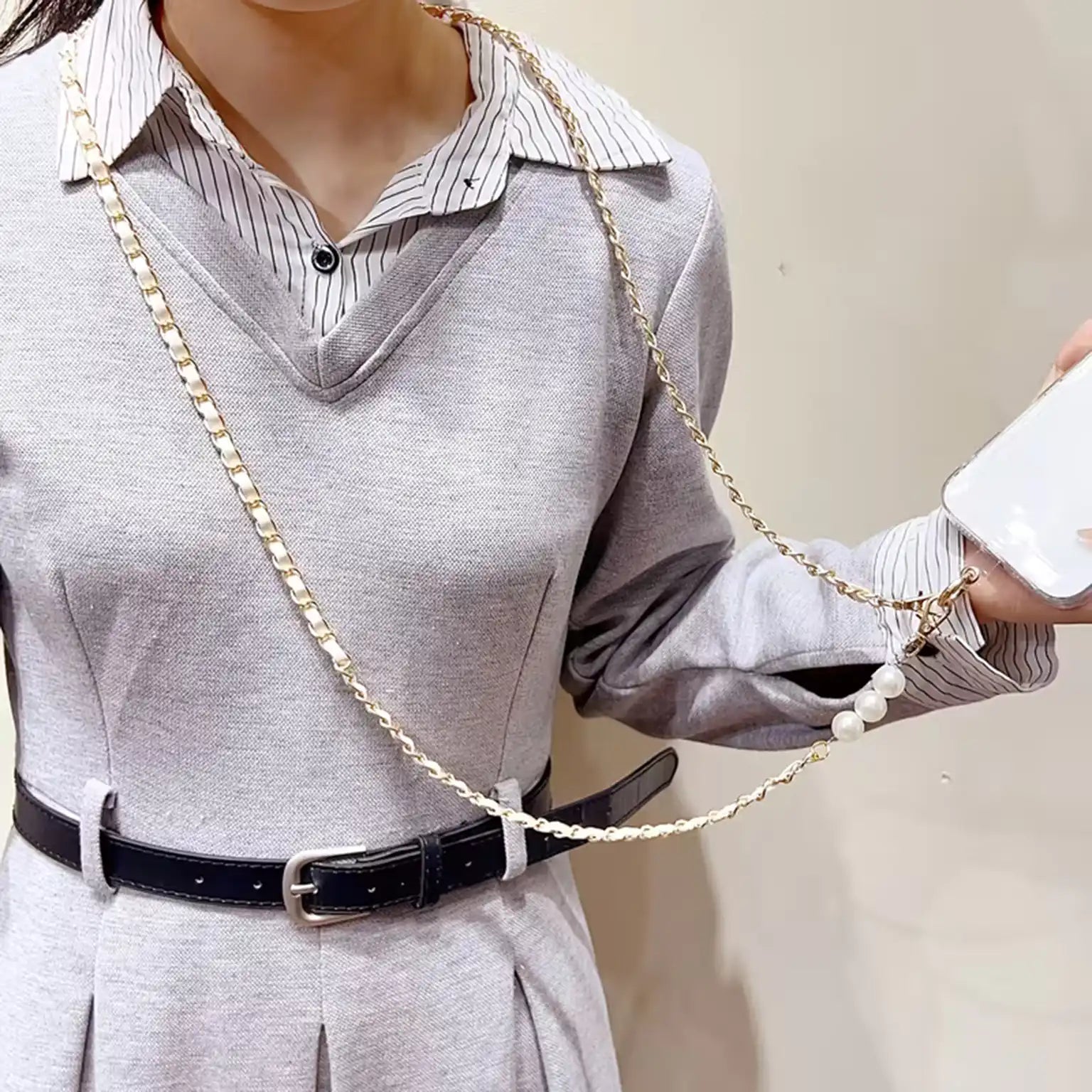 Person wearing a gray outfit with a black belt and a long chain accessory.