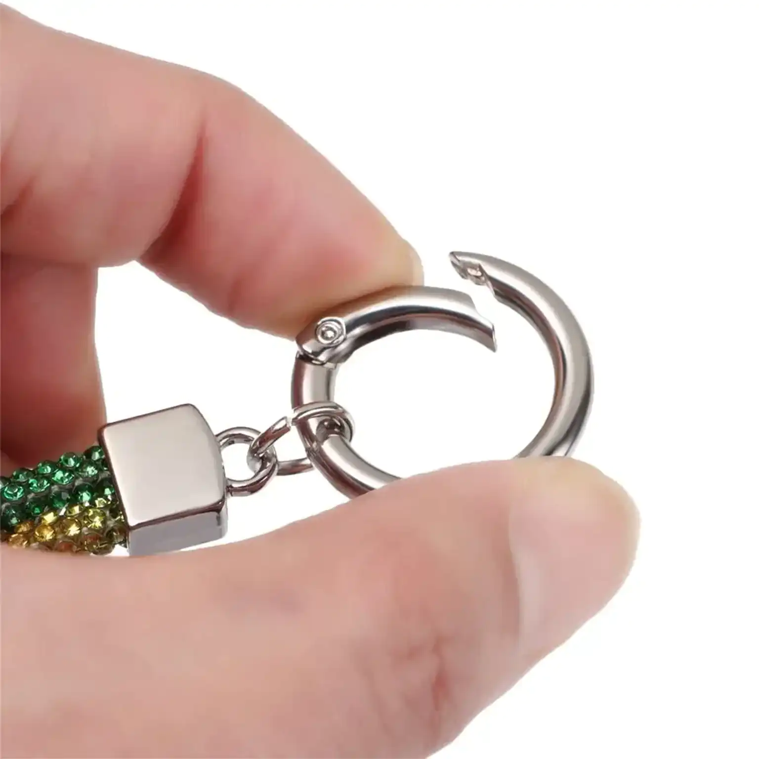 Hand holding a keychain with a silver hook and green gemstones on a white background
