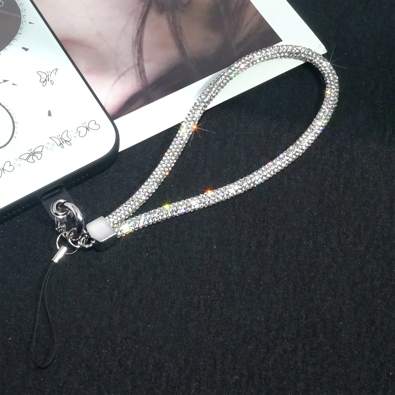 Silver rhinestone phone lanyard on a black surface with a phone in the background.