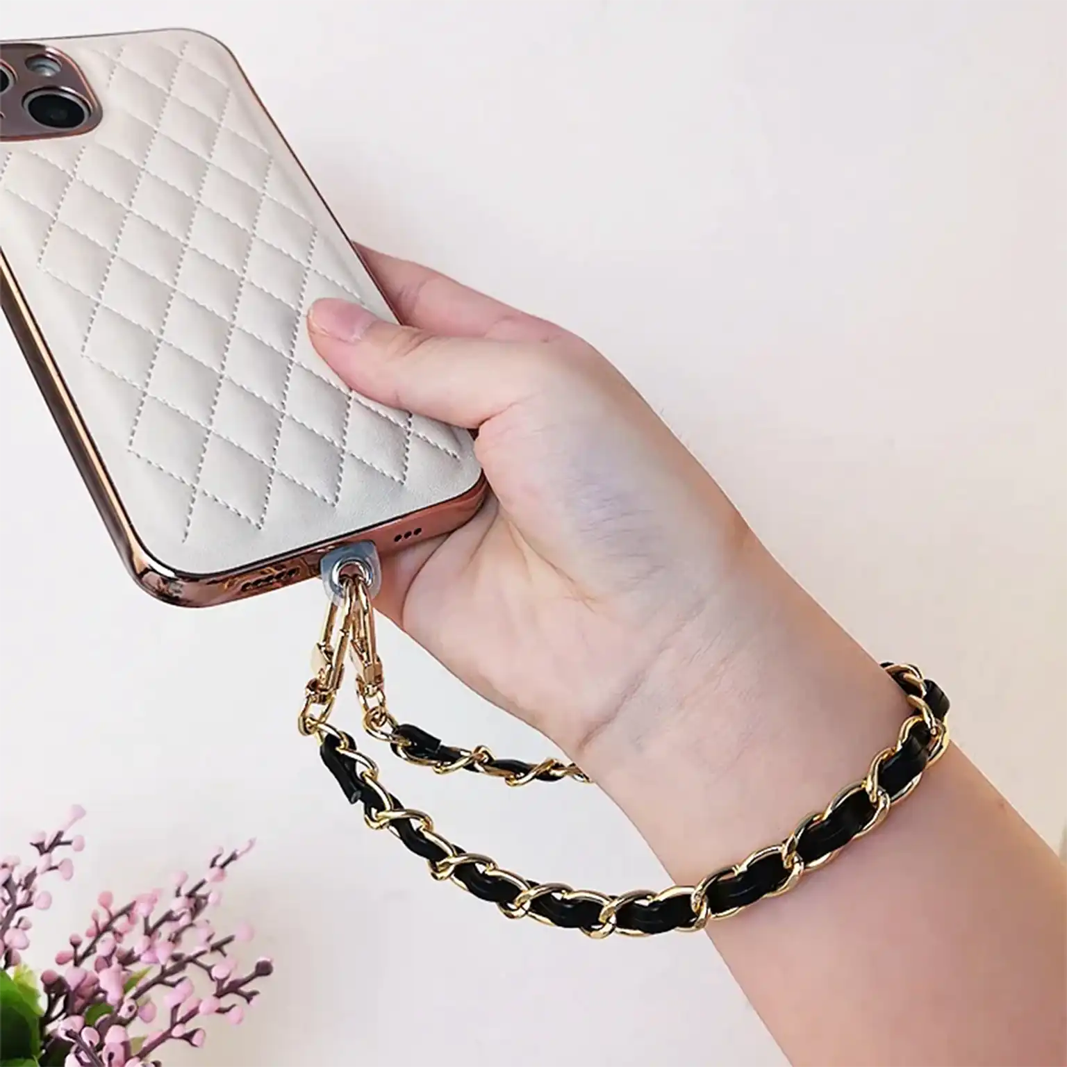 Hand holding a phone with a quilted case and chain strap on a light background