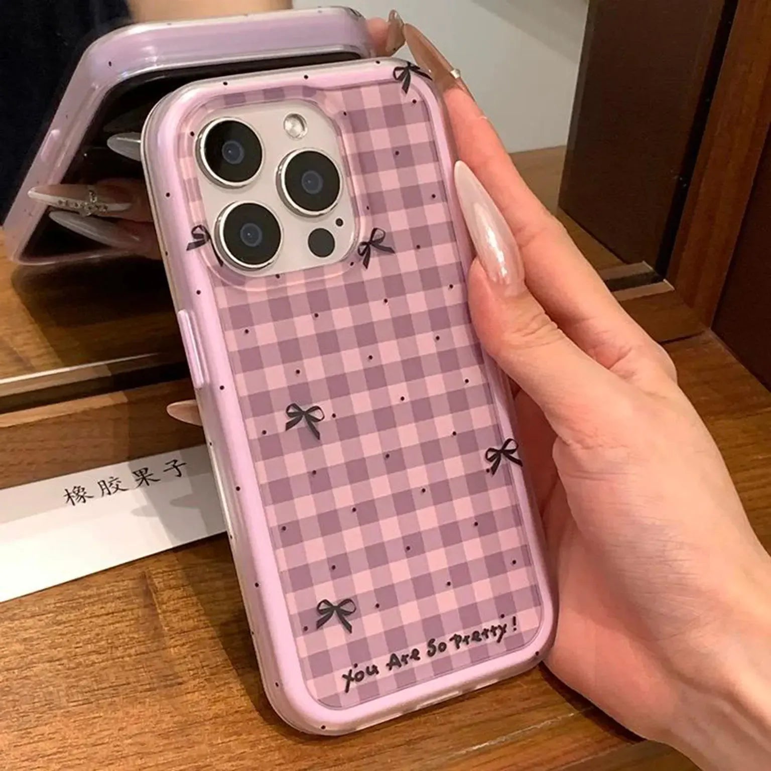 Hand holding a phone case with a purple checkered pattern and bow details.