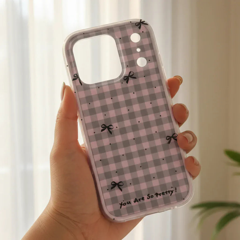 Phone case with checkered pattern and bows held by a hand against a blurred green outdoor background