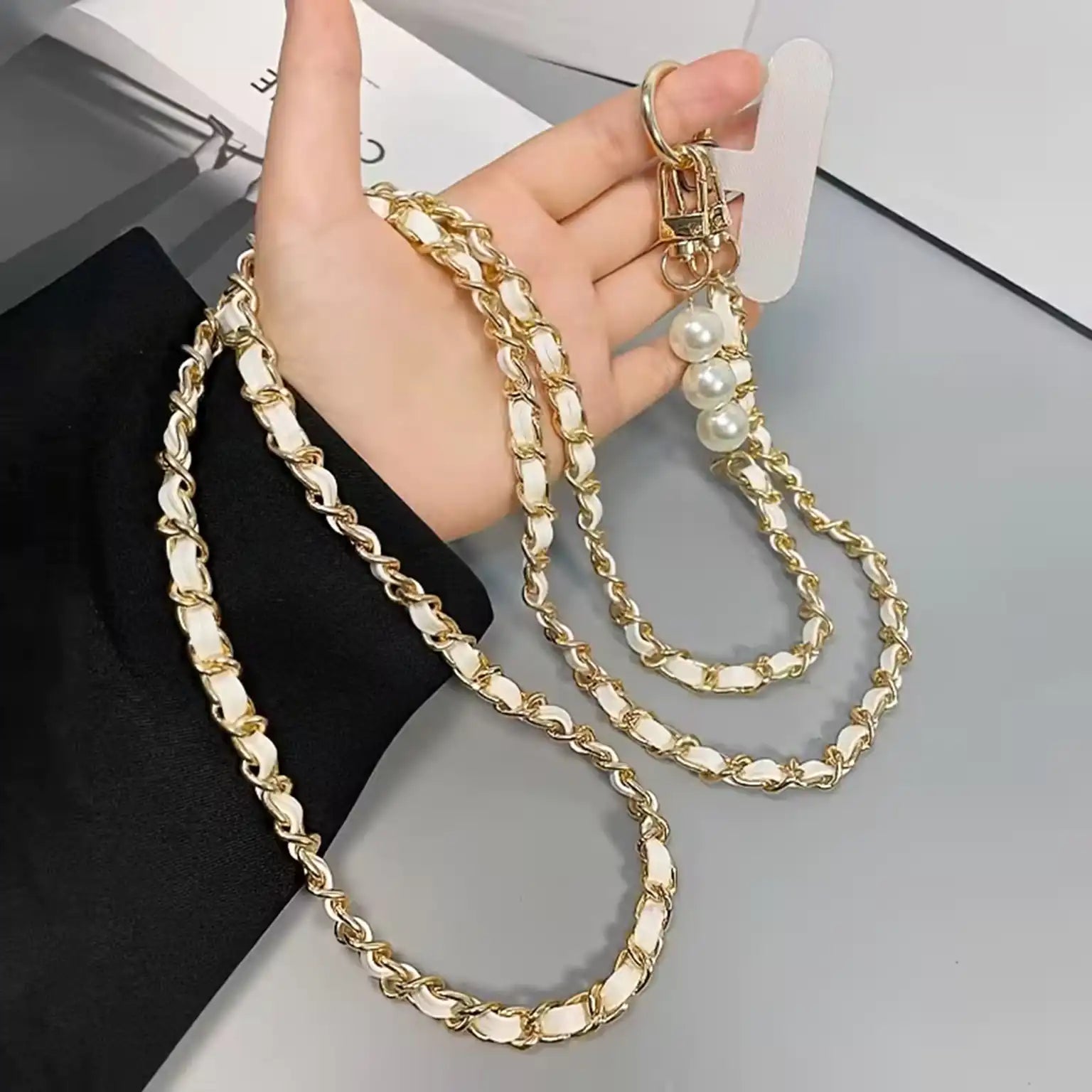 Gold chain with pearl-like beads held by a hand on a gray surface.
