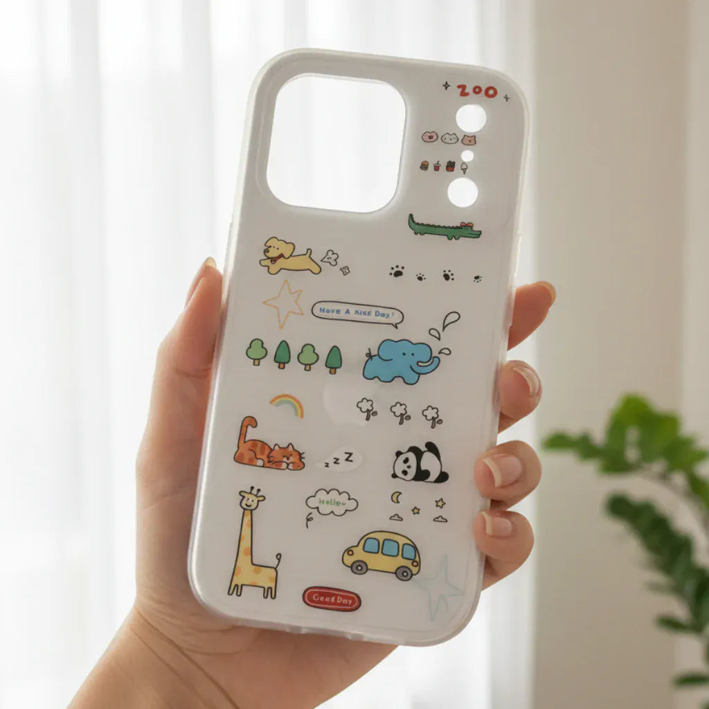 Phone case with cartoon designs held by a hand, outdoors.